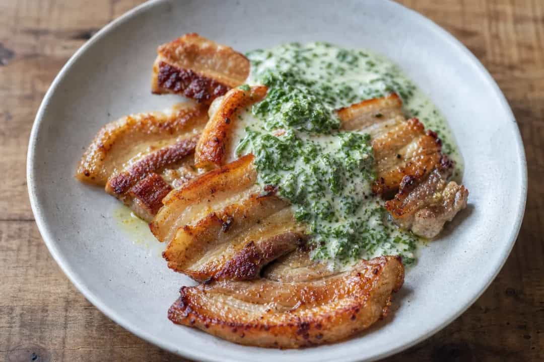 Crispy fried pork belly served with creamy parsley sauce and potatoes, garnished with fresh parsley.