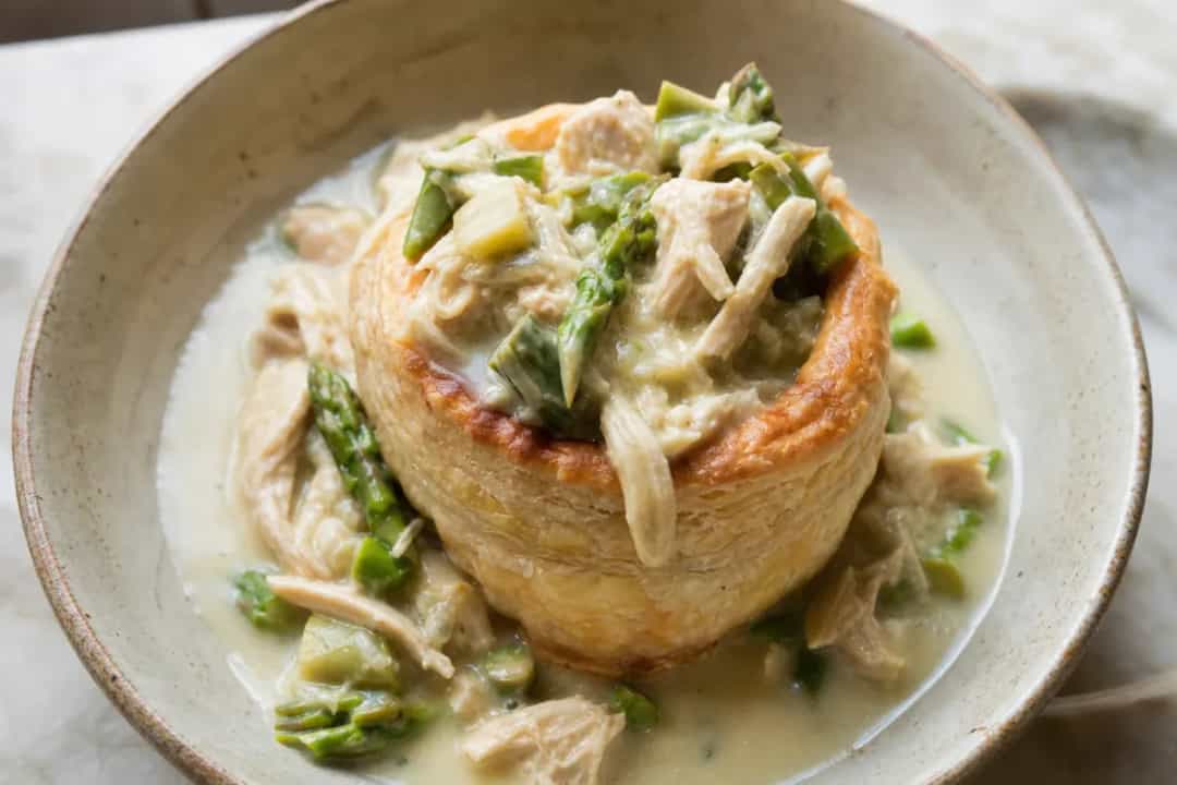 Golden puff pastry filled with creamy chicken and fresh asparagus, garnished with herbs.