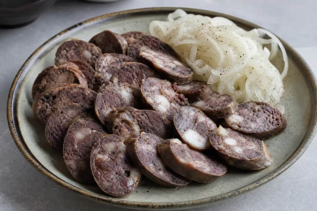 A vibrant platter featuring sliced Kazakh Kazy sausage, garnished with colorful pickled onions and fresh herbs.
