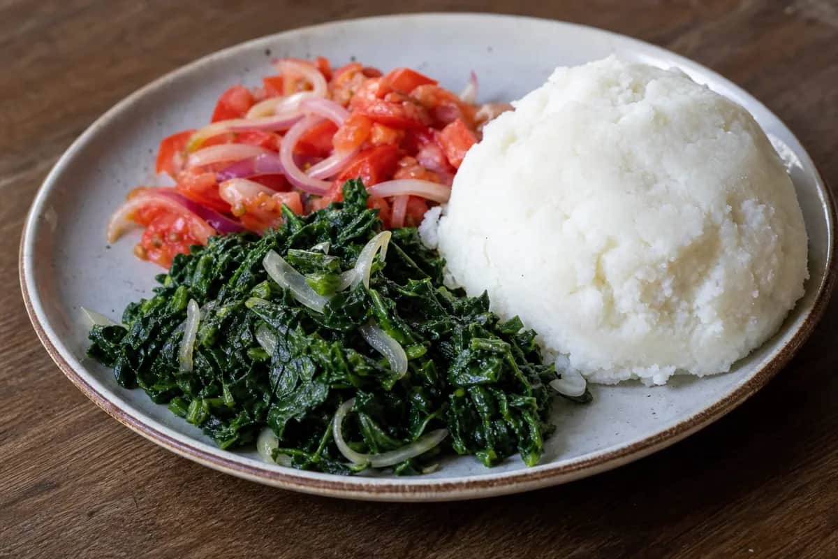 Creamy ugali served with vibrant sukuma wiki and fresh tomato onion relish on a plate.