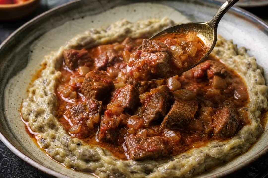 Tender beef stew served over creamy eggplant puree, garnished with parsley.