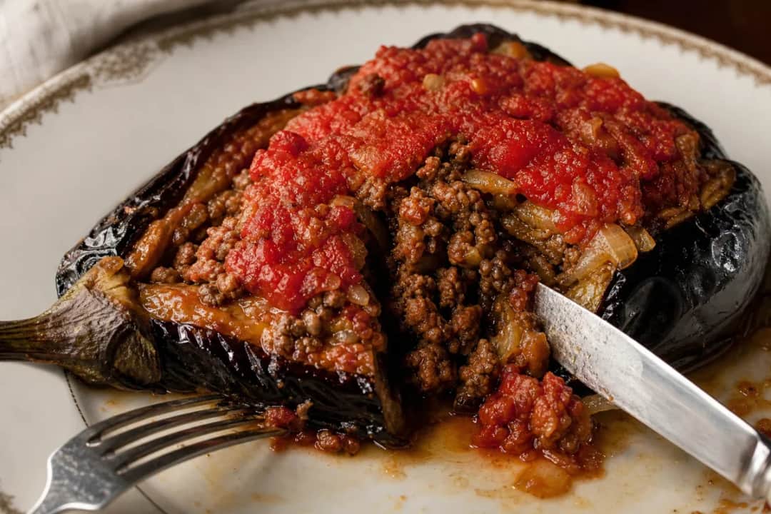 Stuffed eggplant topped with spiced ground meat and fresh herbs, served on a plate.