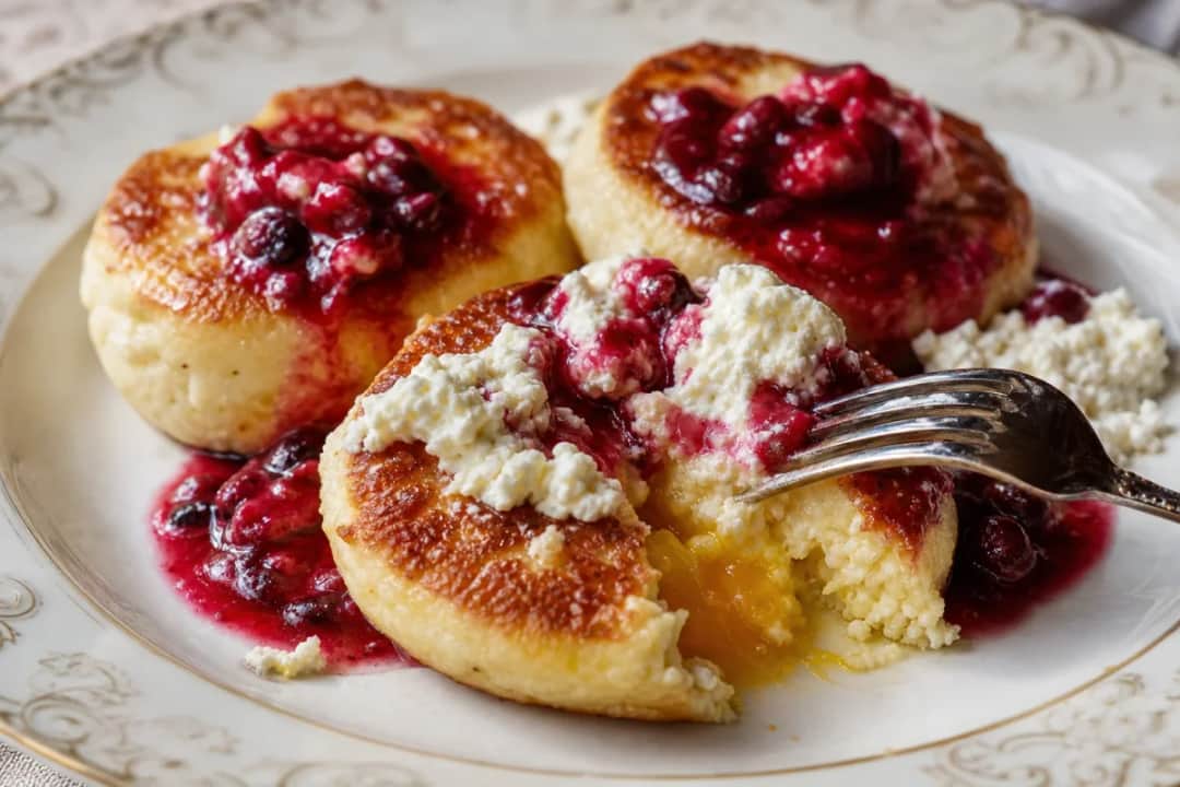 Golden-brown syrniki pancakes topped with vibrant berry sauce and fresh berries