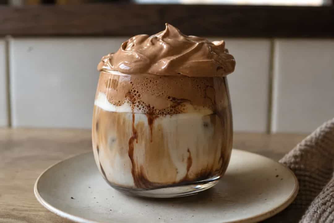 Creamy chocolate iced latte topped with fluffy whipped coffee, served in a clear glass.