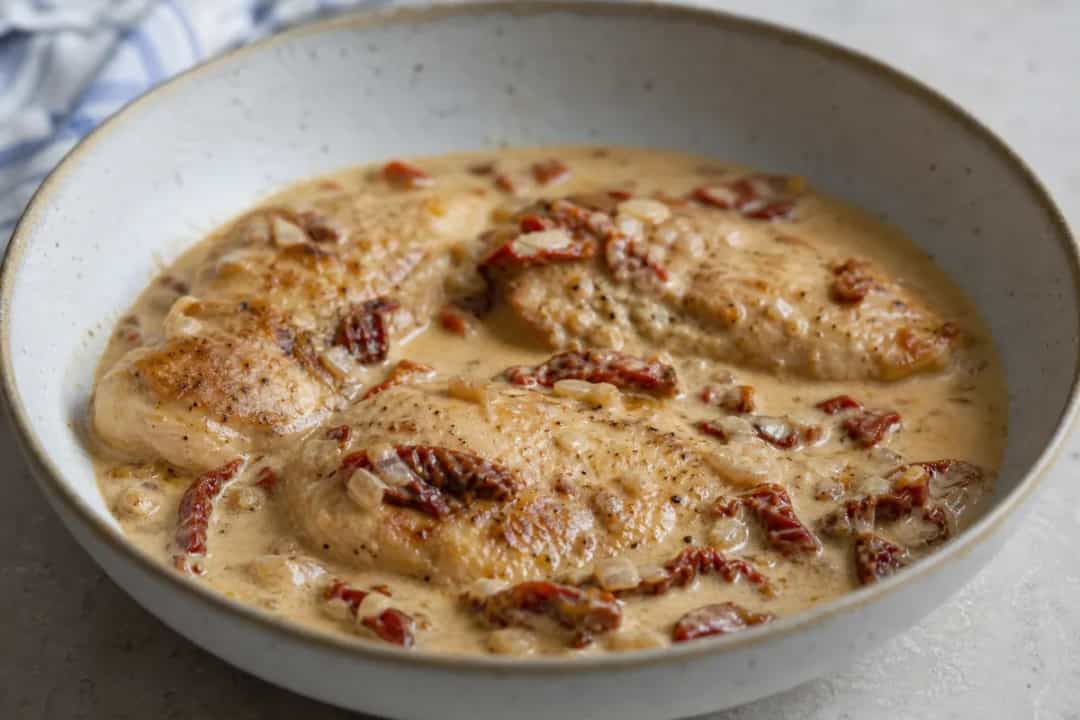 Creamy chicken dish with sun-dried tomatoes, garnished with herbs, served on a plate.