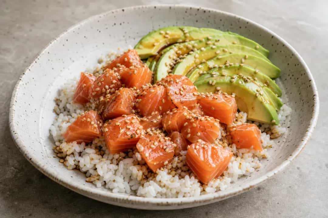 Plated salmon rice bowl with salmon, avocado, and rice topped with sesame seeds.